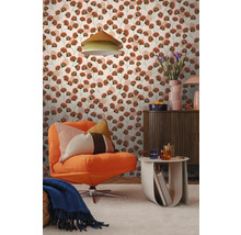 Woonkamer met patroonbehang met gestileerde terracotta en groene bladeren. Met oranje corduroy fauteuil, een houten kast en een bijzettafel.