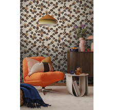 Woonkamer met patroonbehang met gestileerde bruine bladeren, gecombineerd met een oranje fauteuil en een houten dressoir.