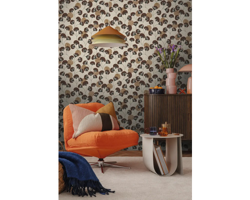 Woonkamer met patroonbehang met gestileerde bruine bladeren, gecombineerd met een oranje fauteuil en een houten dressoir.
