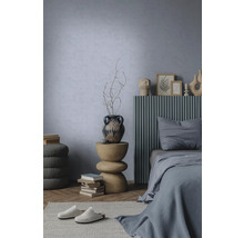 Moderne slaapkamer met lichtblauwe structuurwand, bed met grijs lattenhoofdbord en sculpturale houten bijzettafel.
