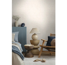 Moderne slaapkamer met een houten stoel, een sculpturale houten bijzettafel, een tafellamp met plissékap en een bed met blauw paneel.