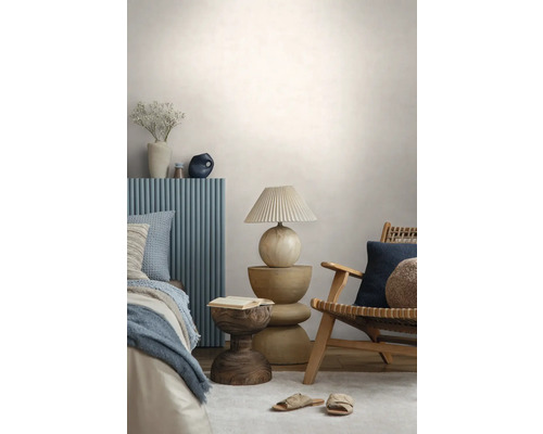 Moderne slaapkamer met een houten stoel, een sculpturale houten bijzettafel, een tafellamp met plissékap en een bed met blauw paneel.