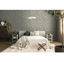 Vliesbehang met bladmotief in een lichte slaapkamer met bed, houten meubels en kamerplanten.