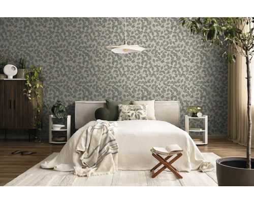 Vliesbehang met bladmotief in een lichte slaapkamer met bed, houten meubels en kamerplanten.