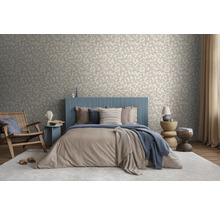 Lichte slaapkamer met behang met bladmotief, bed met blauw hoofdbord met latten, beige beddengoed en houten meubels op een licht tapijt.