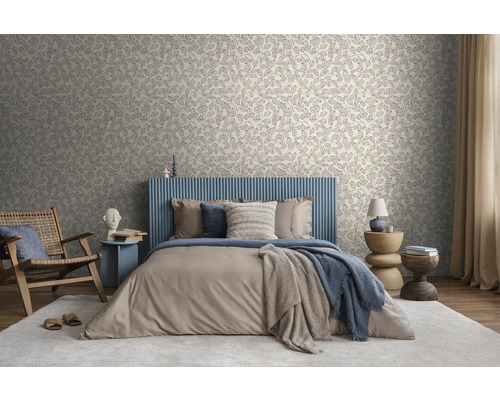 Lichte slaapkamer met behang met bladmotief, bed met blauw hoofdbord met latten, beige beddengoed en houten meubels op een licht tapijt.