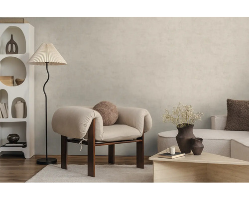 Moderne woonkamer met lichtbeige muurverf in betonlook, lichte fauteuil, vloerlamp en witte designkast op houten vloer.
