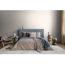 Moderne slaapkamer met blauw geribbeld hoofdbord, beige beddengoed, houten stoel en licht vloerkleed tegen een lichtgrijze muur.
