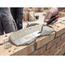 Hand brengt met een metselaarstroffel mortel aan op een bakstenen muur op een bouwplaats.