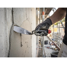 Een vakman brengt met een troffel mortel aan op een betonnen muur op een lichte en georganiseerde bouwplaats.