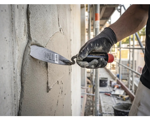 Een vakman brengt met een troffel mortel aan op een betonnen muur op een lichte en georganiseerde bouwplaats.