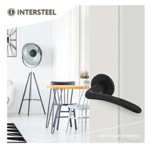 Intersteel Logo. Zwarte deurkruk op een witte deur in een lichte, modern ingerichte kamer met tafel, stoelen en vloerlamp.