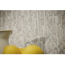 Vliesbehang met gestructureerd steenpatroon in grijs en beige met een subtiel silhouet van een kan.