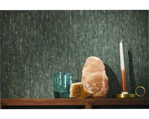 Donkergroen vliesbehang met een verticale structuur op een wand achter een houten plank met een zoutlamp kaars en glas.