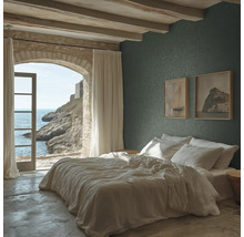 Slaapkamer met donkergroen structuurbehang, wit bed, plafond met houten balken en een stenen boog met uitzicht op zee.