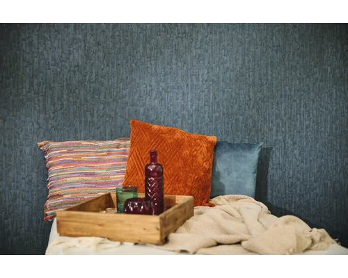 Blauw behang met structuur in een kamer met decoratieve kussens in oranje, blauw en meerkleurig, een houten dienblad en een deken.