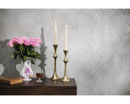Grijs vliesbehang met vintage-structuur en subtiel patroon in een klassiek ingerichte scène met kandelaars, bloemen en een boek.