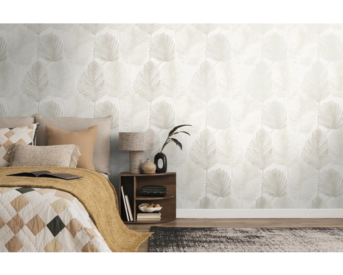 Lichte slaapkamer met vliesbehang met palmbladmotief, een bed met kussens en een nachtkastje met lamp.