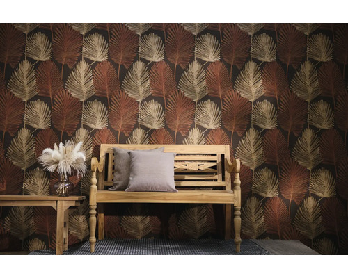 Vliesbehang met een patroon van grote palmbladeren in aardetinten achter een houten bank met kussens en een bijzettafel.
