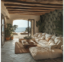 Lichte woonkamer in mediterrane stijl met grote bank, houten plafondbalken, natuurstenen vloer, behang met bladmotief en uitzicht op zee.