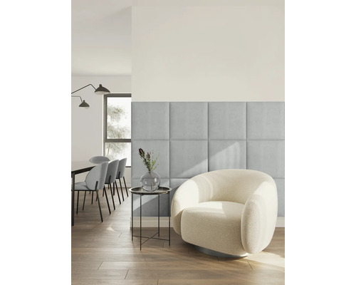 Moderne, lichte woonkamer met vierkante, beklede wandpanelen van lichtblauwe stof naast een ronde fauteuil van witte bouclé-stof.