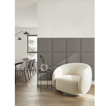 Moderne woonkamer met grijze gestoffeerde wandpanelen, een lichte fauteuil en een eethoek op de achtergrond.