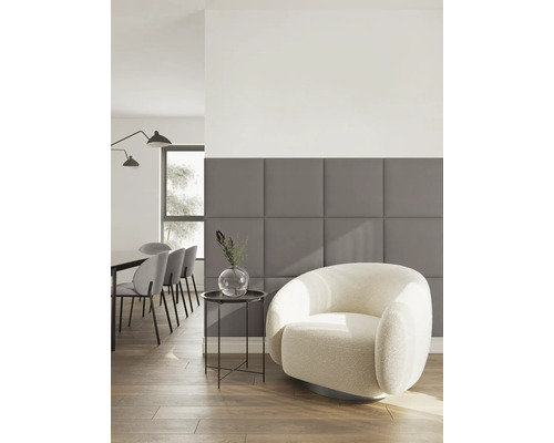 Moderne woonkamer met grijze gestoffeerde wandpanelen, een lichte fauteuil en een eethoek op de achtergrond.