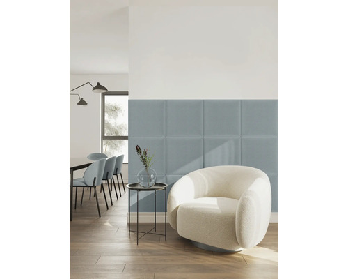 Vierkante gestoffeerde wandpanelen van stof in blauw in een lichte, modern ingerichte woonkamer met een witte fauteuil en houten vloer.