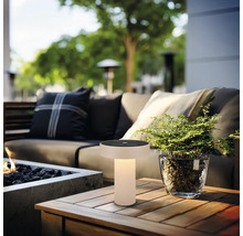 Moderne solar tafellamp voor buiten met warm licht op een houten tafel in een loungehoek met bank en plant.