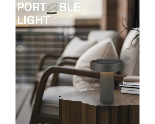 Moderne draagbare LED-tafellamp op een houten tafel in een buitenruimte met fauteuils.