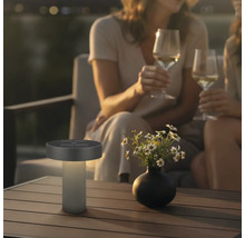 Moderne LED-tafellamp op zonne-energie voor buiten op een houten tafel in een gezellige avondtuin met mensen.