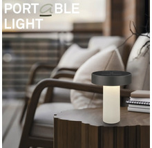 Draagbare LED-tafellamp op een houten tafel in een moderne buitenruimte met comfortabele fauteuils.