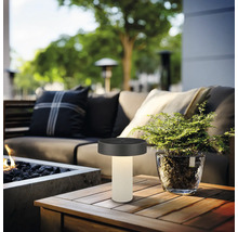Moderne LED-tafellamp voor buiten op een houten tafel in een gezellige zithoek met vuurkorf en planten.
