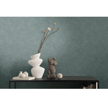 Getextureerd vliesbehang in petrol achter een zwarte console met decoratieve vazen en sculpturen.