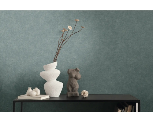 Getextureerd vliesbehang in petrol achter een zwarte console met decoratieve vazen en sculpturen.