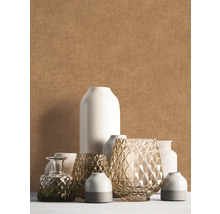 Effen gestructureerd behang in beige achter een decoratieve groep van diverse witte en glazen vazen.