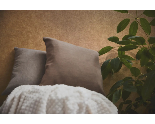Twee sierkussens en een deken met textuur voor behang met patroon naast een kamerplant.