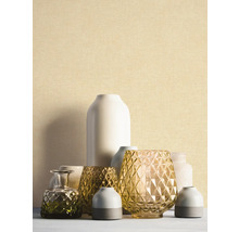 Fijn gestructureerd behang in lichtbeige achter een groep decoratieve vazen van glas en keramiek.