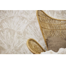 Behang met structuur en een groot waaiervormig palmbladpatroon achter een fauteuil van rotanvlechtwerk met een stoffen kussen.