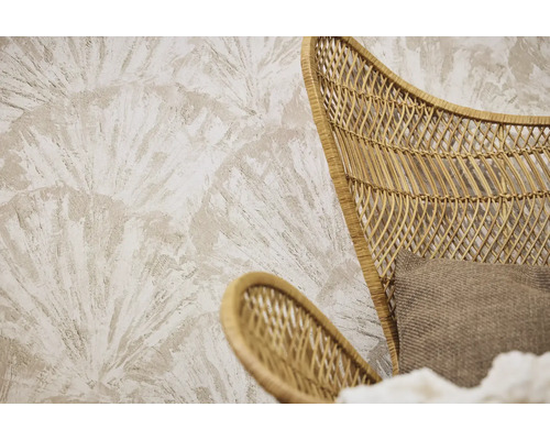 Behang met structuur en een groot waaiervormig palmbladpatroon achter een fauteuil van rotanvlechtwerk met een stoffen kussen.