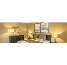 Moderne slaapkamer met donkere commode, bed met kussens en twee schilderijen aan de wand, sfeervol verlicht door diverse lampen.