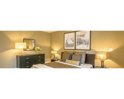 Moderne slaapkamer met donkere commode, bed met kussens en twee schilderijen aan de wand, sfeervol verlicht door diverse lampen.