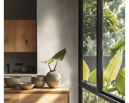 Lichte moderne keuken met houten kasten, keramieken kommen en vaas op een houten oppervlak voor een groot raam met uitzicht op groene planten.