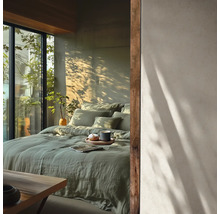 Lichte slaapkamer met groen linnen beddengoed op het bed, grote ramen en schaduwen van planten op de muur. Minimalistische stijl.