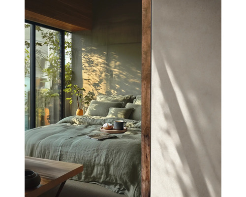 Lichte slaapkamer met groen linnen beddengoed op het bed, grote ramen en schaduwen van planten op de muur. Minimalistische stijl.