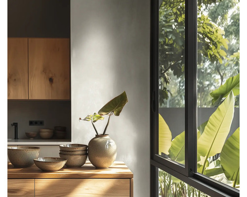 Lichte keuken met houten kasten, keramische kommen en een vaas op een houten werkblad voor een groot raam met uitzicht op planten.