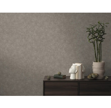 Gestructureerd vliesbehang in betonlook op een muur achter een donker dressoir met boeken en een plant in een pot.