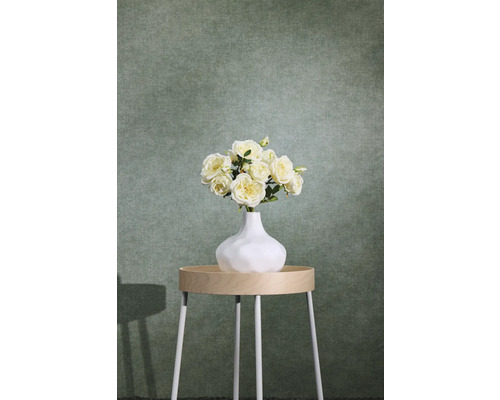 Groen gestructureerd vliesbehang met textieloptiek achter een bijzettafel met bloemenvaas.