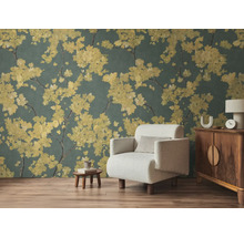 Vliesbehang met gele bloesemtakken op donkere achtergrond in woonkamer met lichte fauteuil en houten meubels op laminaatvloer.