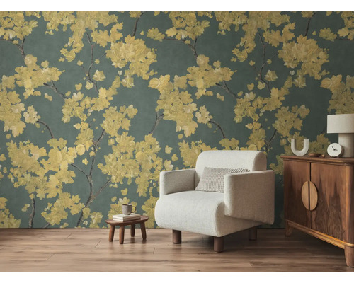 Vliesbehang met gele bloesemtakken op donkere achtergrond in woonkamer met lichte fauteuil en houten meubels op laminaatvloer.